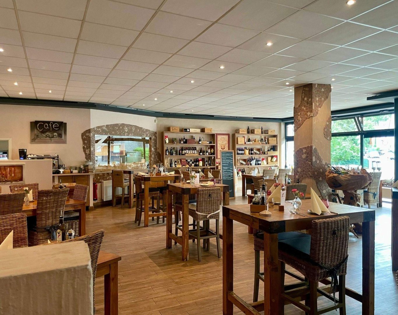 Heller Restaurantbereich mit Holzmöbeln und Regalen voller Bücher.