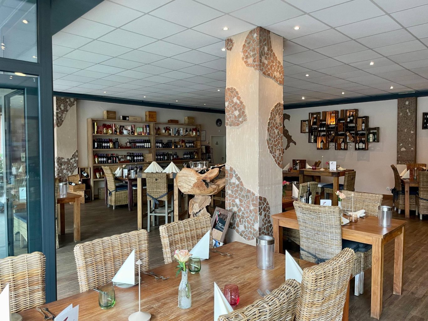 Ein helles Restaurant mit Holztischen, Stühlen und dekorativen Regalen.