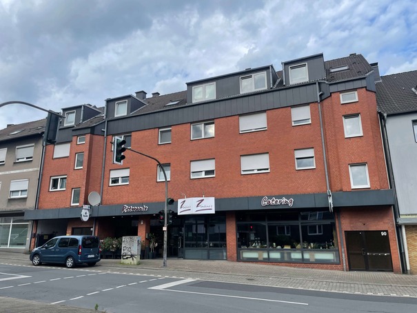 Dreigeschossiges rotes Wohngebäude mit Geschäften im Erdgeschoss und grauem Dach.